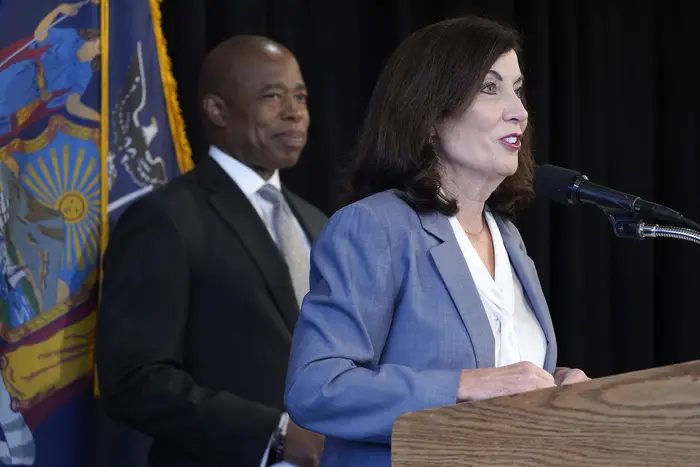Gov. Kathy Hochul speaks at a podium while Mayor Eric Adams stands in the background.